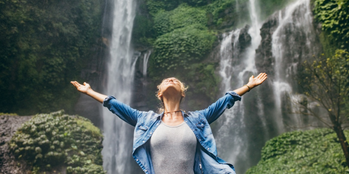 Donna che apre le braccia davanti a una cascata, simbolo di libertà e crescita personale.